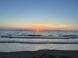 Tramonto sul mare, cielo azzurro e una strscia arancione nel mezzo, con il sole riflesso sulle onde.